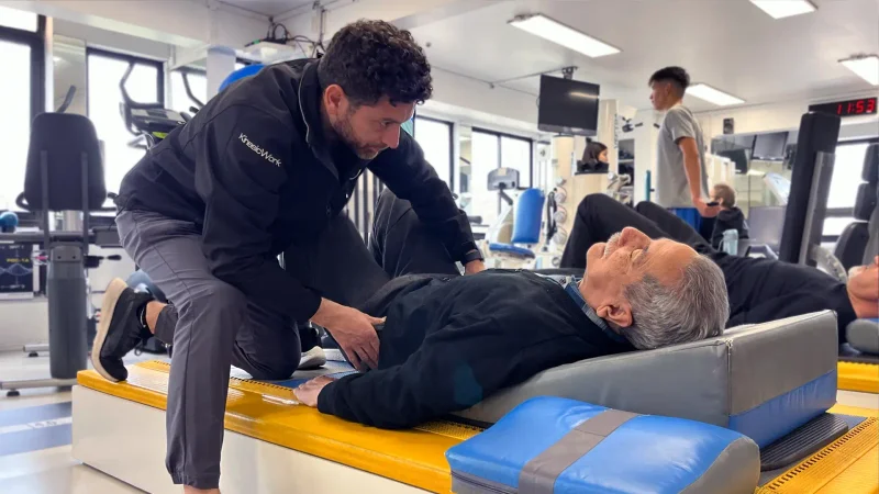 Kinesiólogo asistiendo a un paciente adulto mayor recostado en camilla durante sesión de kinesiología en KinesicWork
